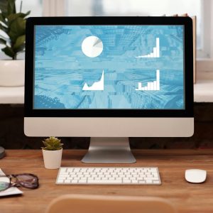 Stylish home office setup with desktop, plant, and eyeglasses on a wooden desk.
